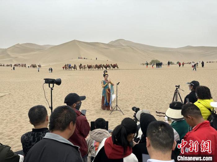 圖為2023年4月底，敦煌大漠“逐舞者”奧楠在鳴沙山月牙泉景區(qū)視頻直播，吸引游人圍觀?！●T志軍 攝